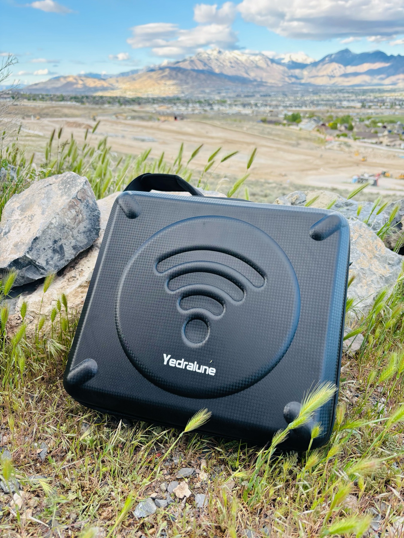 Yedralune hard-shell carrying case for Starlink Mini resting on rocks with mountain view