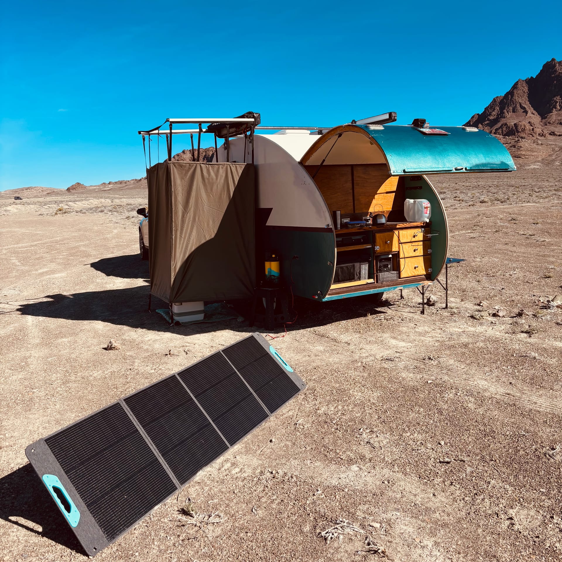 Pearl teardrop camper with galley open and solar panel deployed in the desert, mountains behind