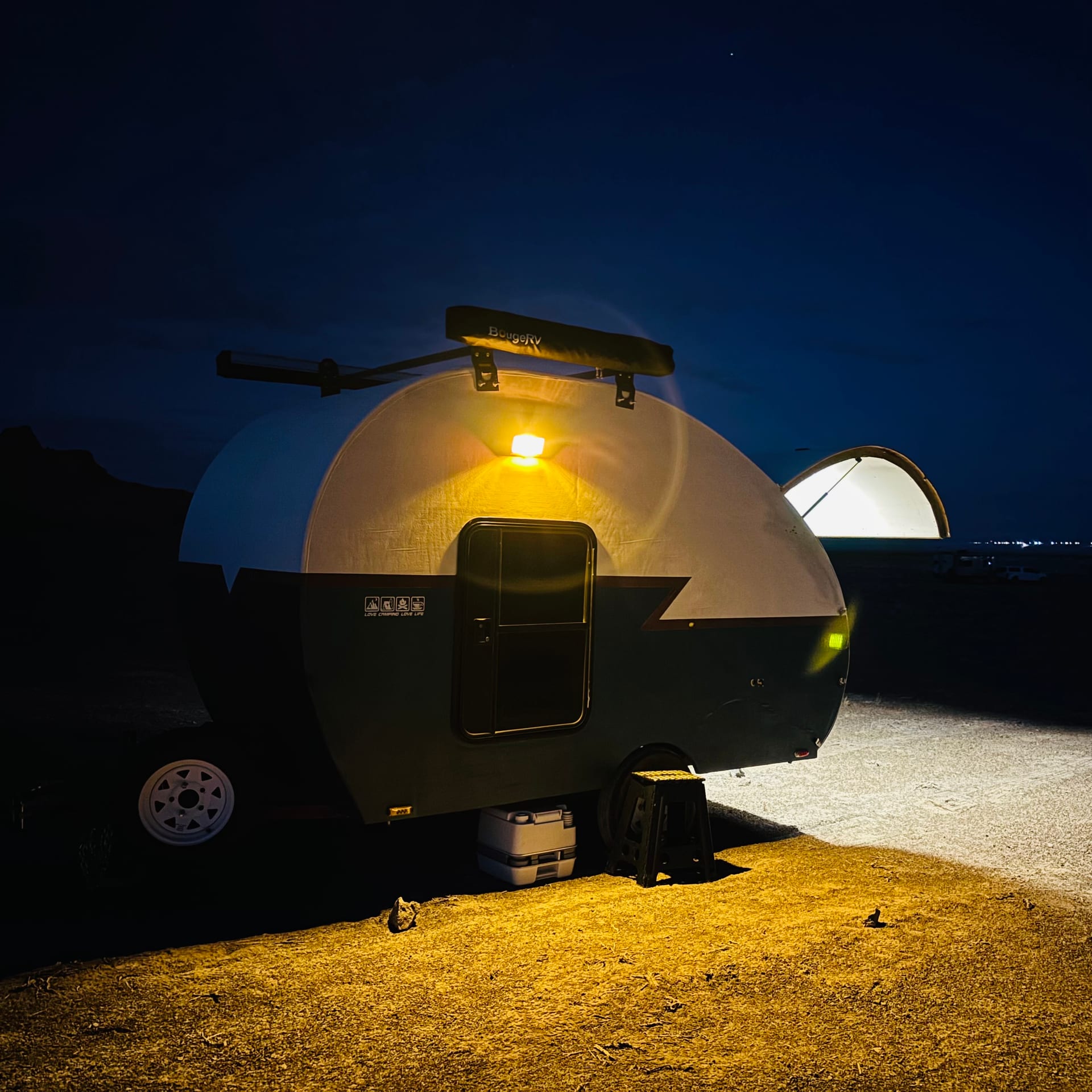 Pearl teardrop camper set up at the dispersed campsite with side light glowing in the desert evening